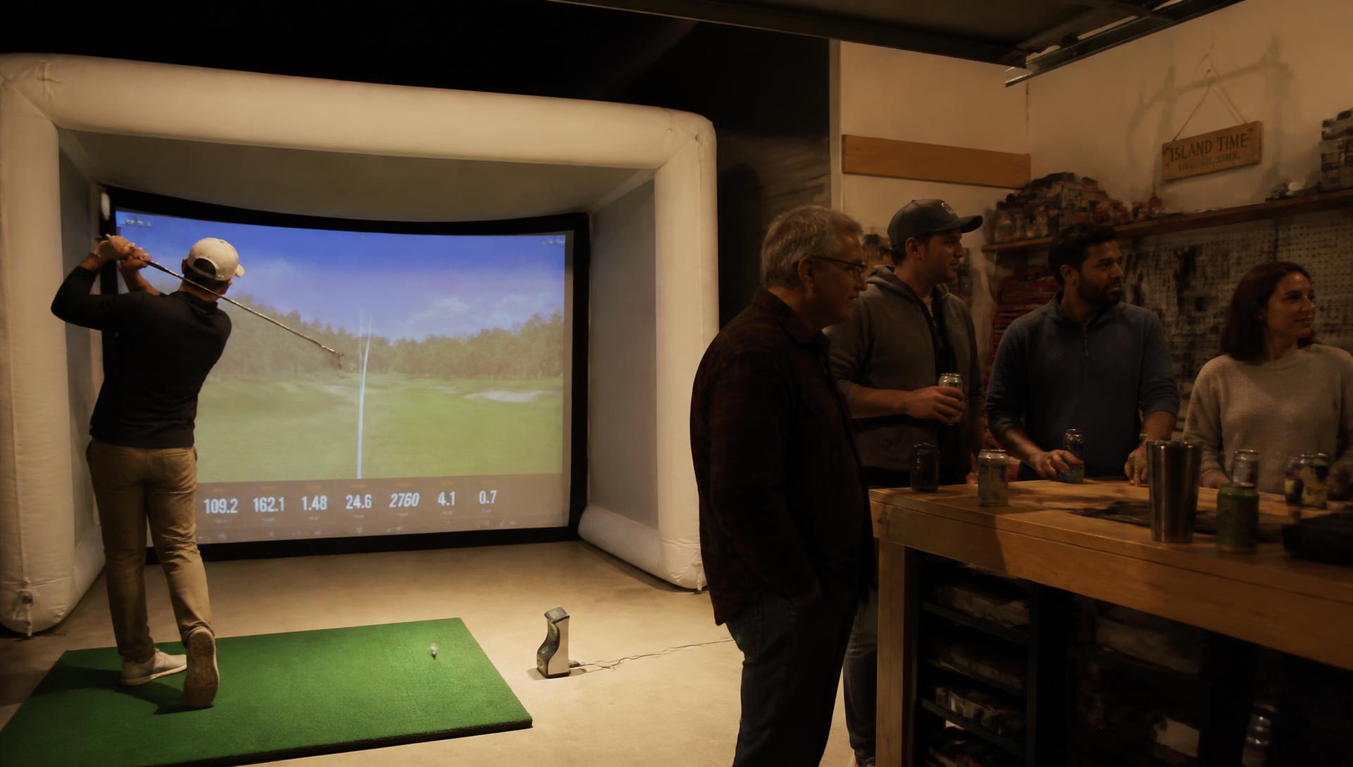 Golfer mid-swing inside the HomeDrop Golf inflatable simulator at night
